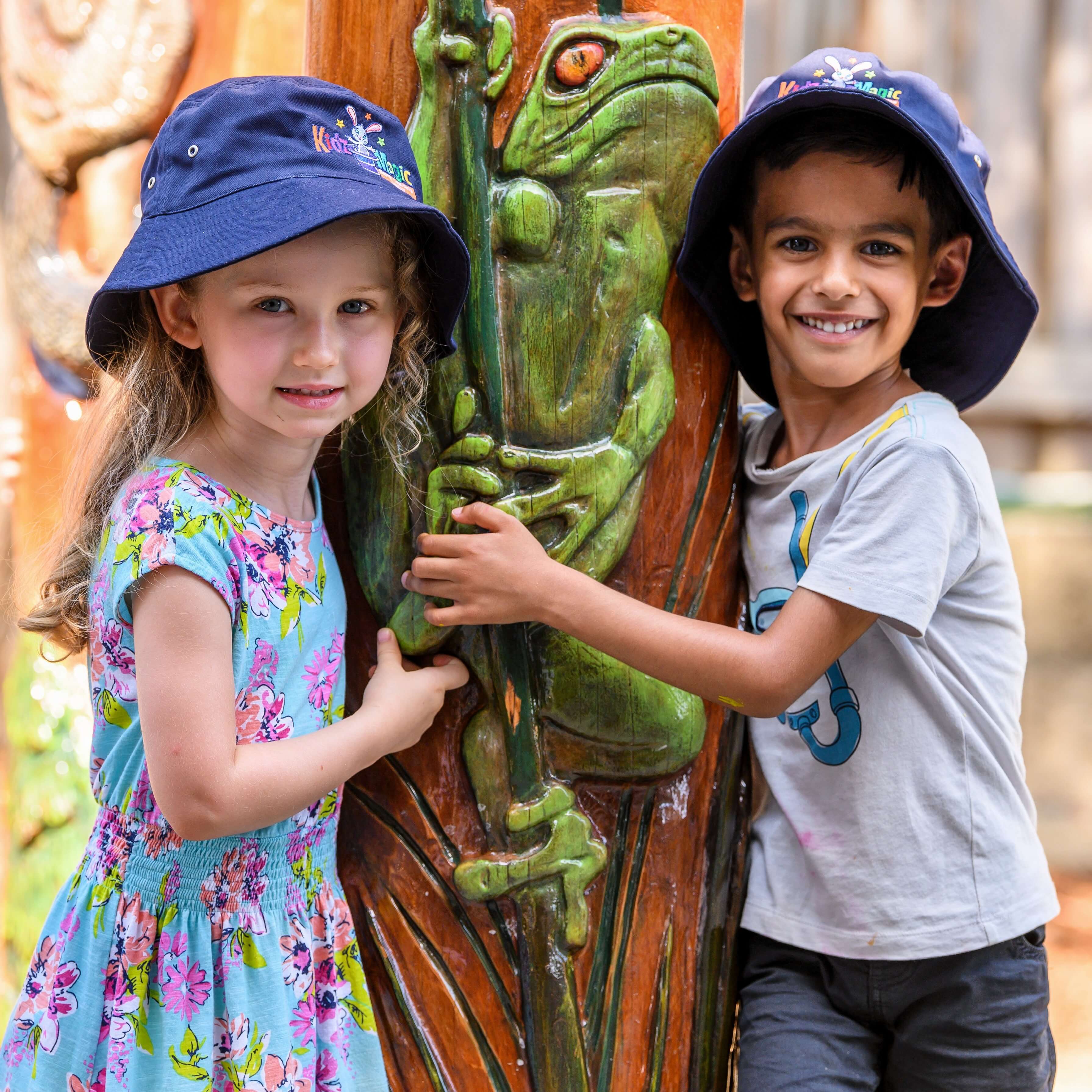 Two children in a playground, next to a pillar with a frog drawn on it.